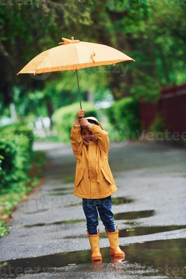 Niño Con Paraguas De Colores, Vestido Con Capa Impermeable Amarilla Y Botas  De Pie Bajo La Lluvia. Niño Caminando En La Ducha De Otoño. Fotos,  retratos, imágenes y fotografía de archivo libres