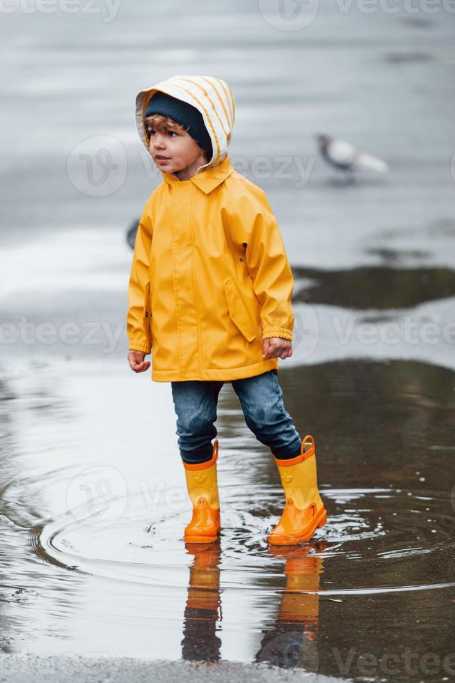 niño con capa impermeable amarilla y botas jugando al aire libre