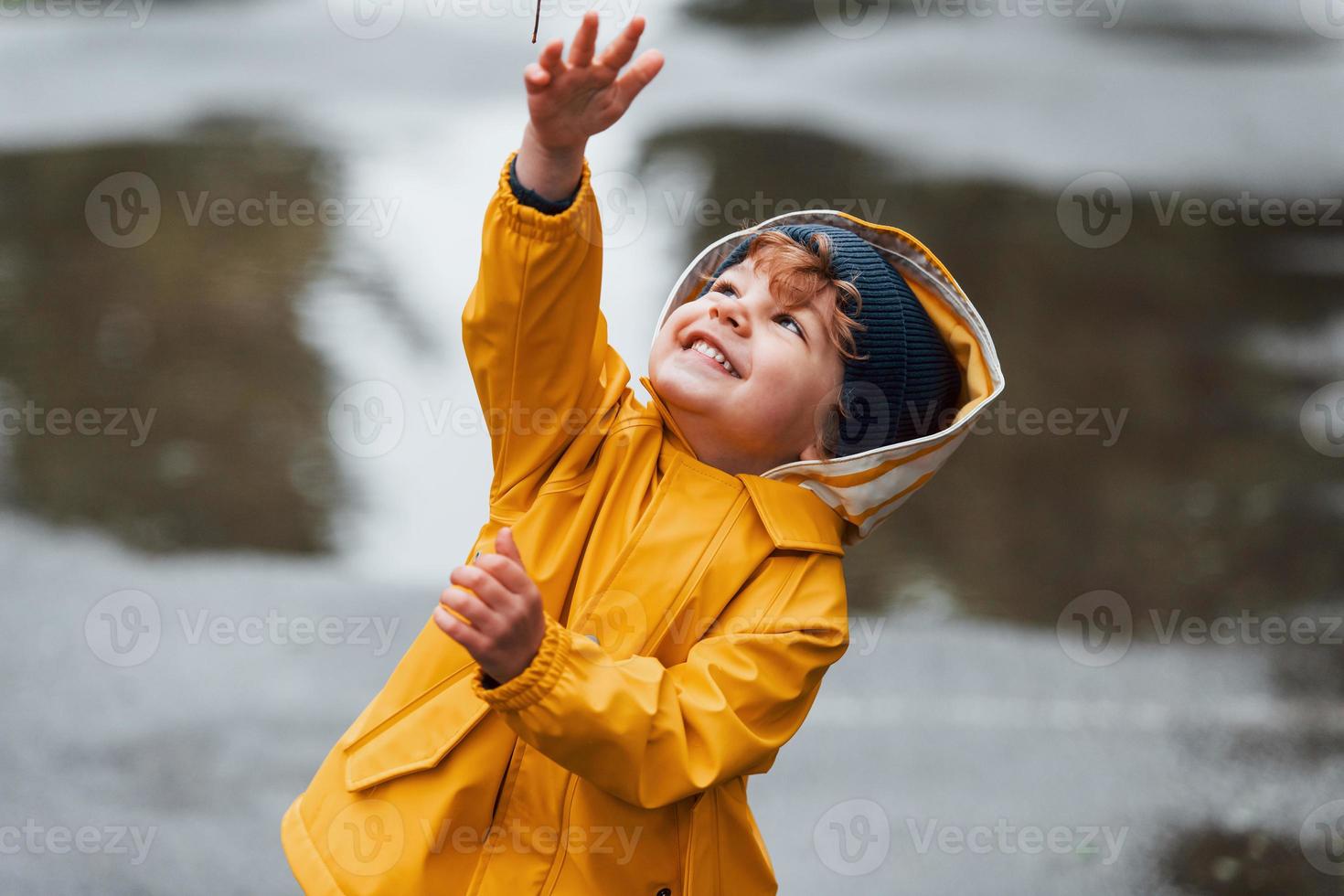 Kid in yellow waterproof cloak and boots playing outdoors after the rain photo