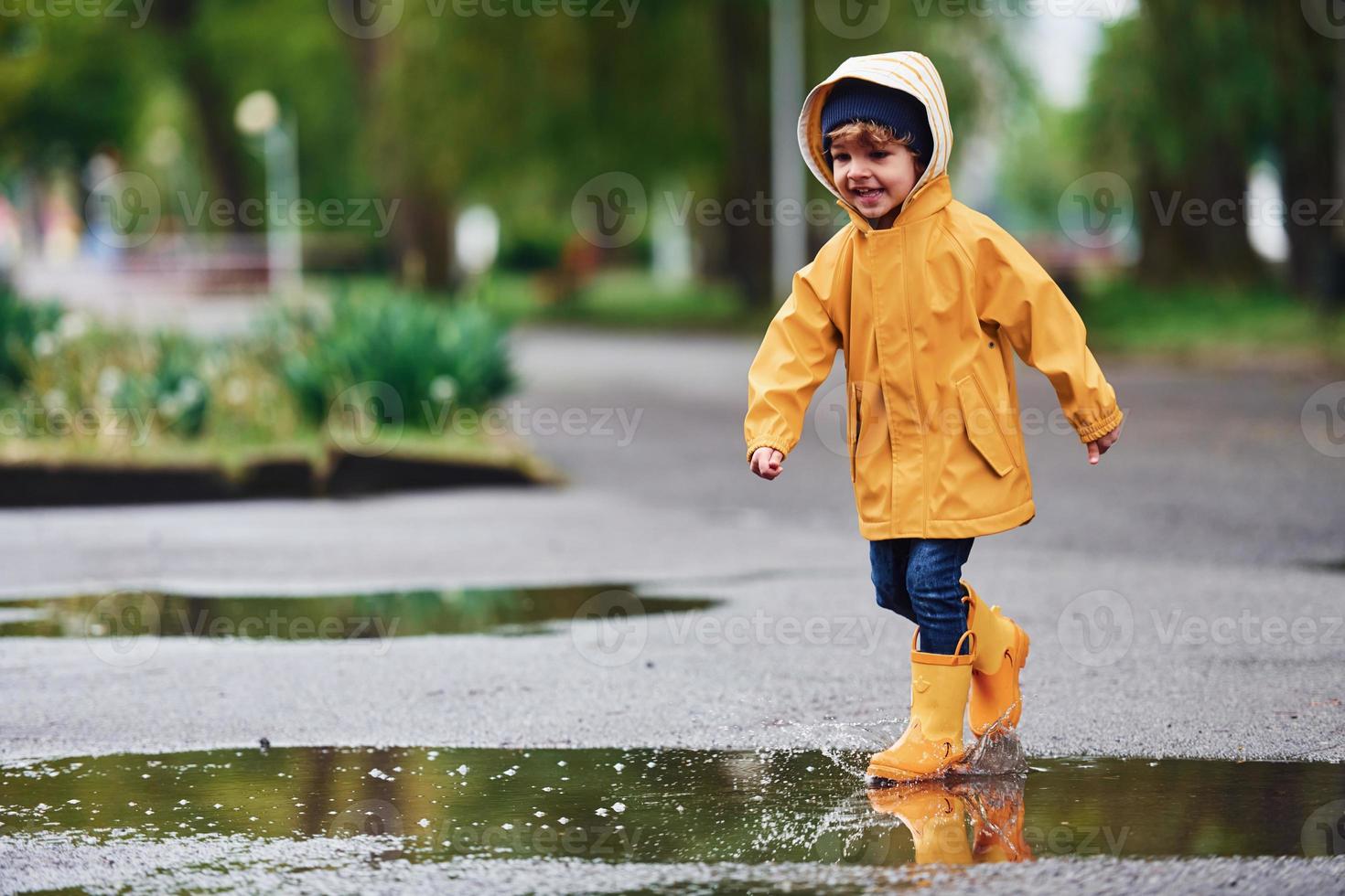 niño con capa impermeable amarilla y botas jugando al aire libre después de  la lluvia 15290534 Foto de stock en Vecteezy