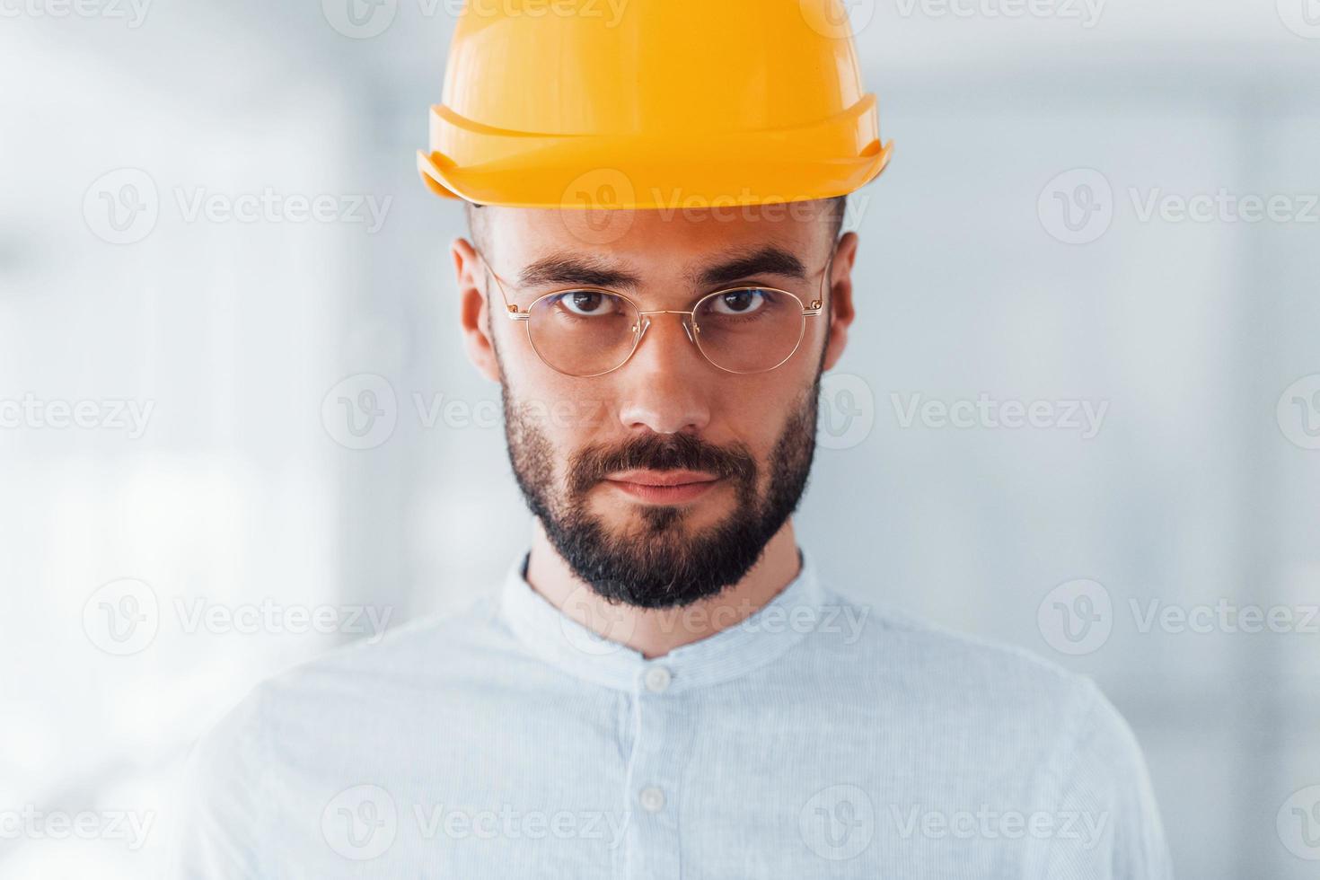 Portrait of engineer in orange protective hard hat and glasses that standing and working indoors photo