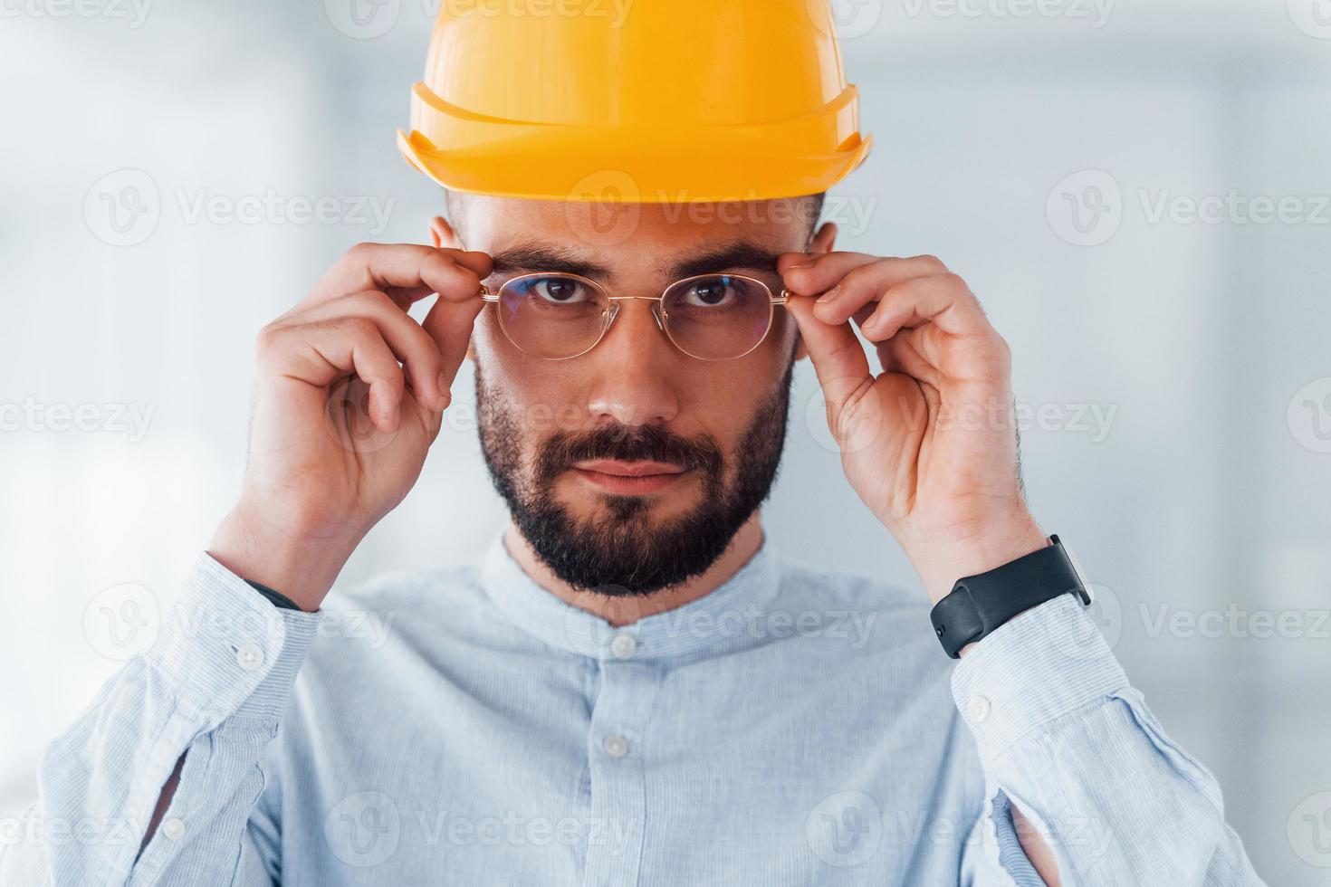 retrato de ingeniero con casco protector naranja y anteojos que están parados y trabajando en interiores foto