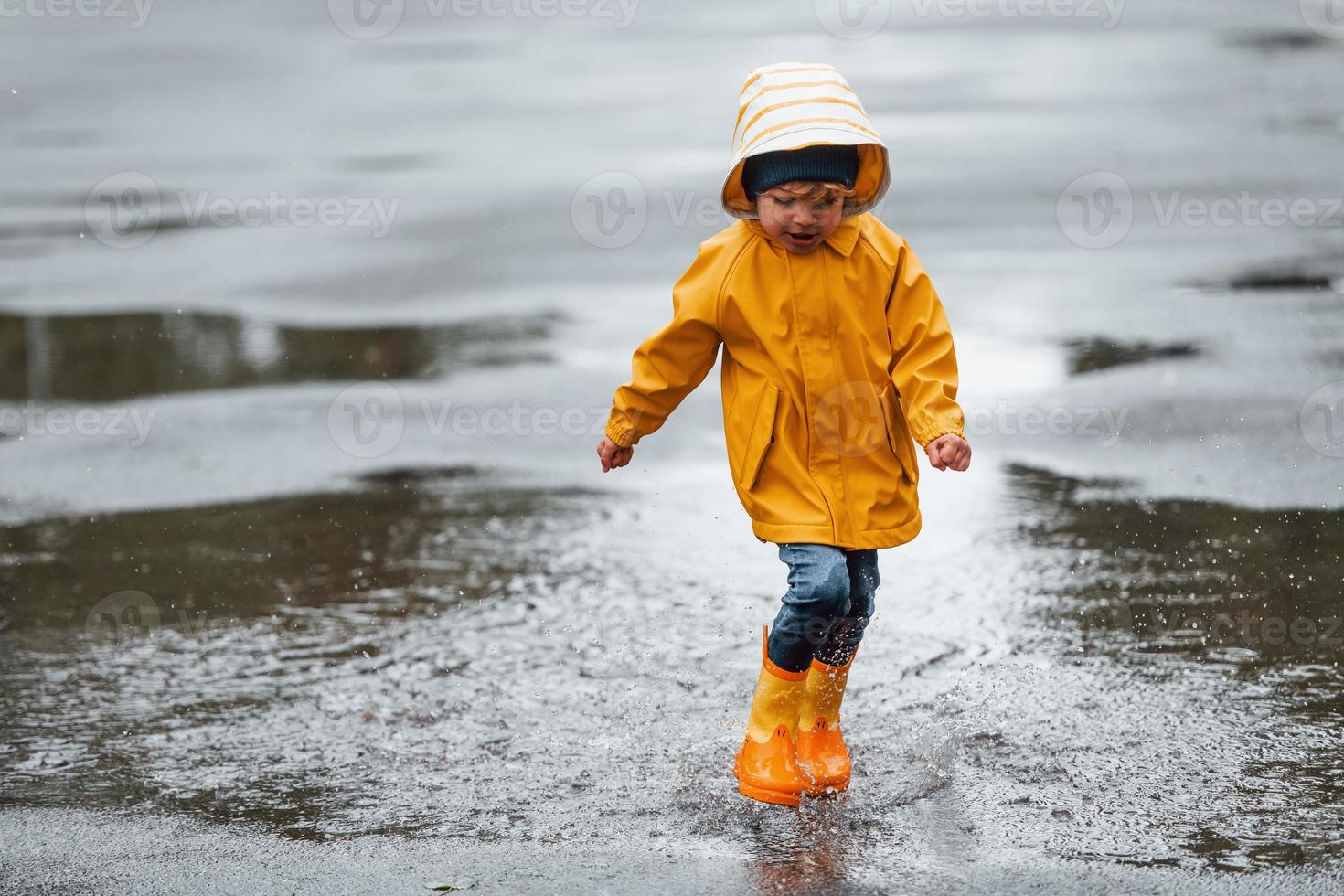 Kid in yellow waterproof cloak and boots playing outdoors after the rain photo