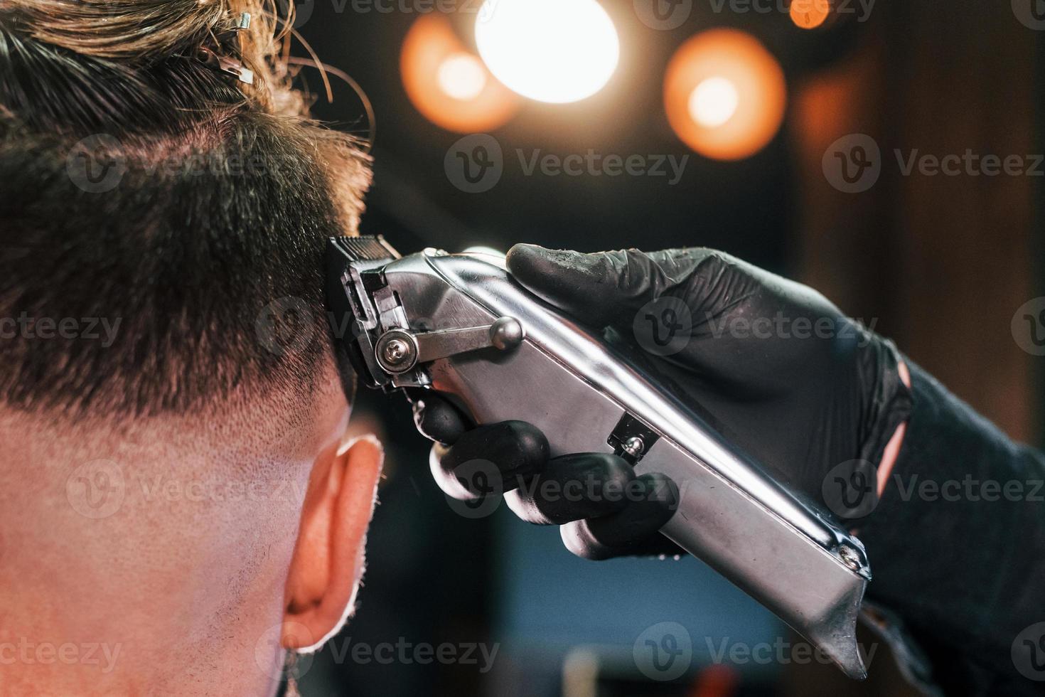 Close up view of young bearded man that sitting and getting haircut in barber shop photo