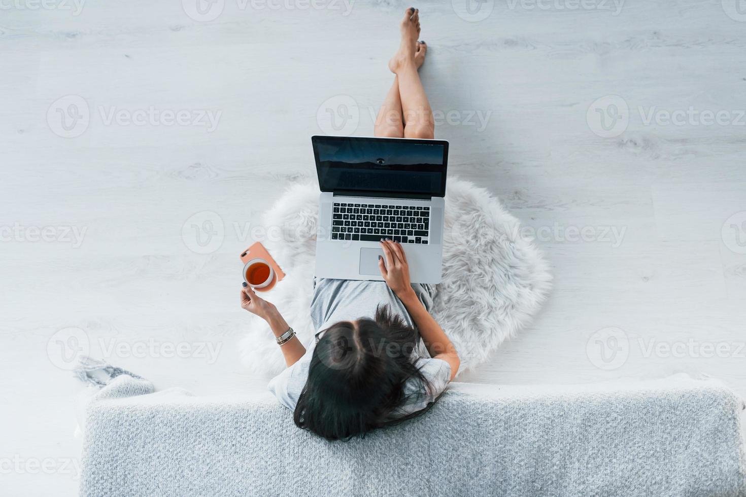 Top view of young woman in casual clothes that sitting at home alone with laptop and tea photo