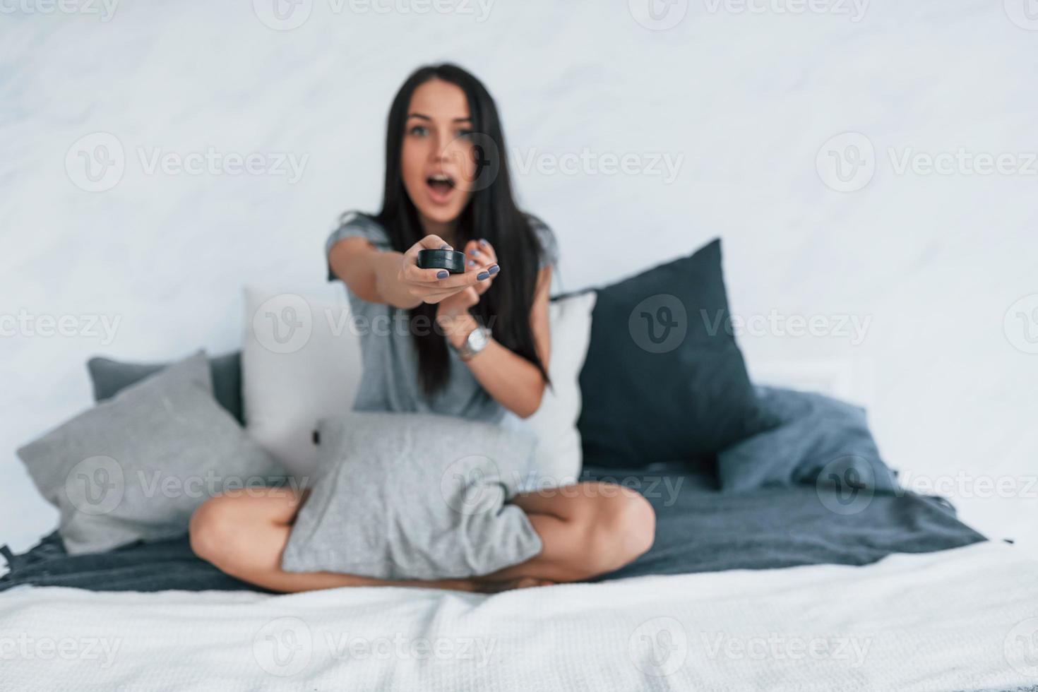 Holding TV remote and watching movie. Young beautiful woman in casual clothes sitting at home alone photo