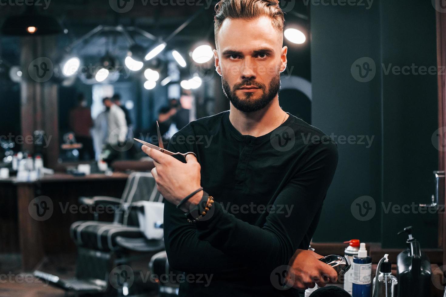 joven barbudo parado en una barbería y sosteniendo unas tijeras foto