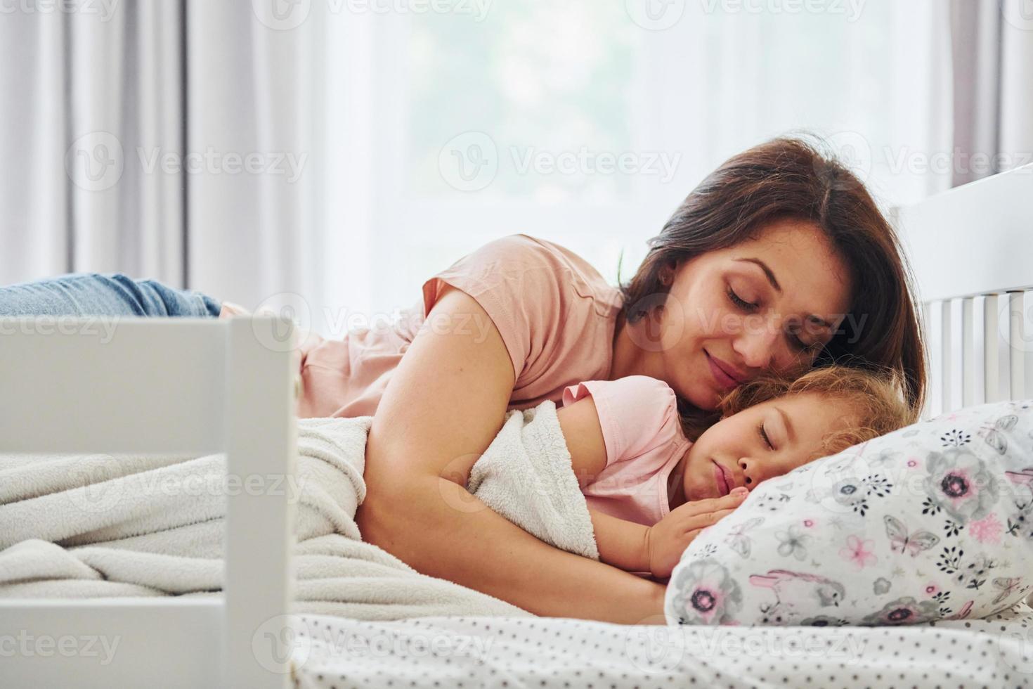 Sleep time. Young mother with her little daughter in casual clothes together indoors at home photo