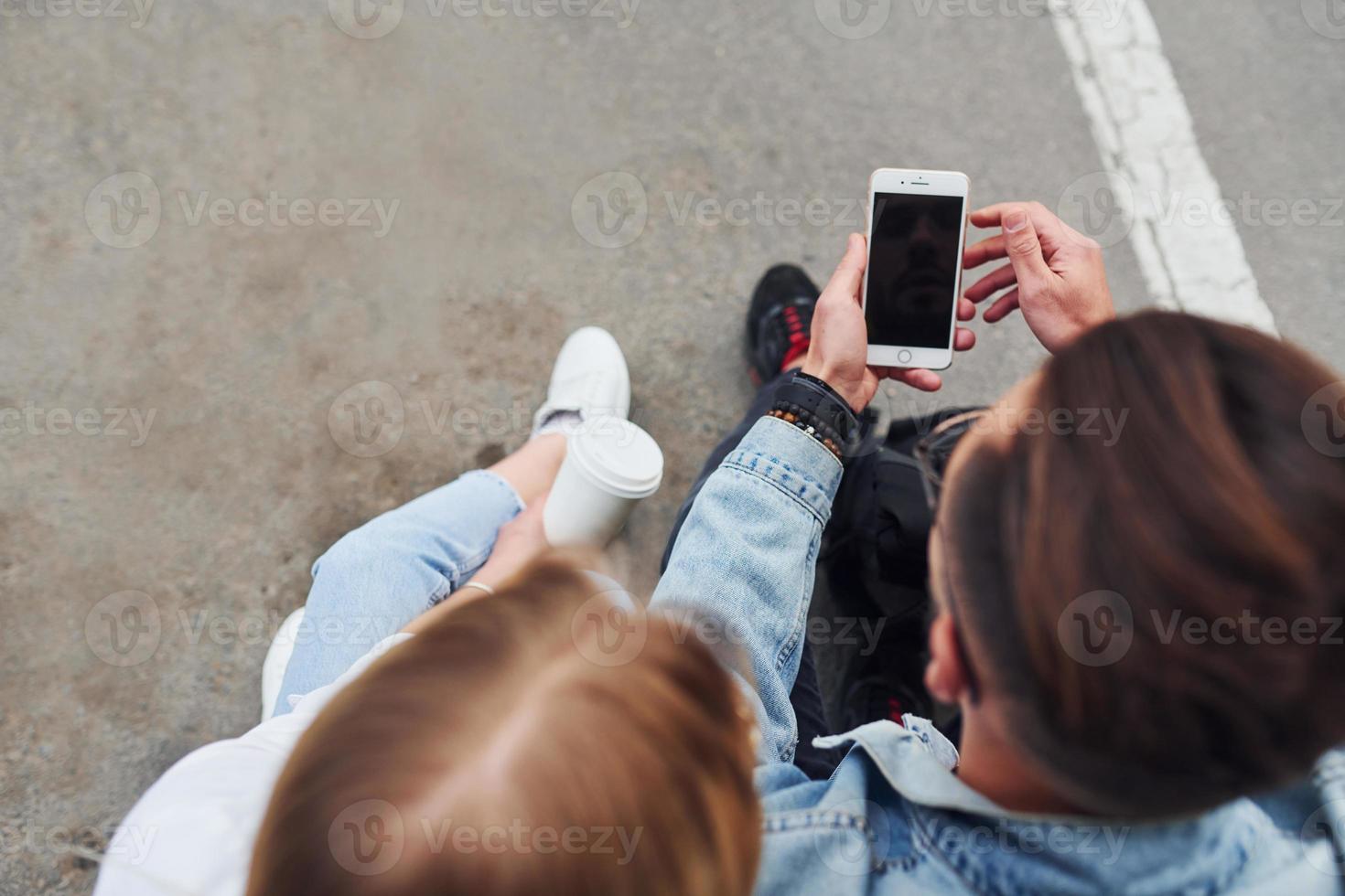 Using phone. Young stylish man with woman in casual clothes sitting outdoors together. Conception of friendship or relationships photo