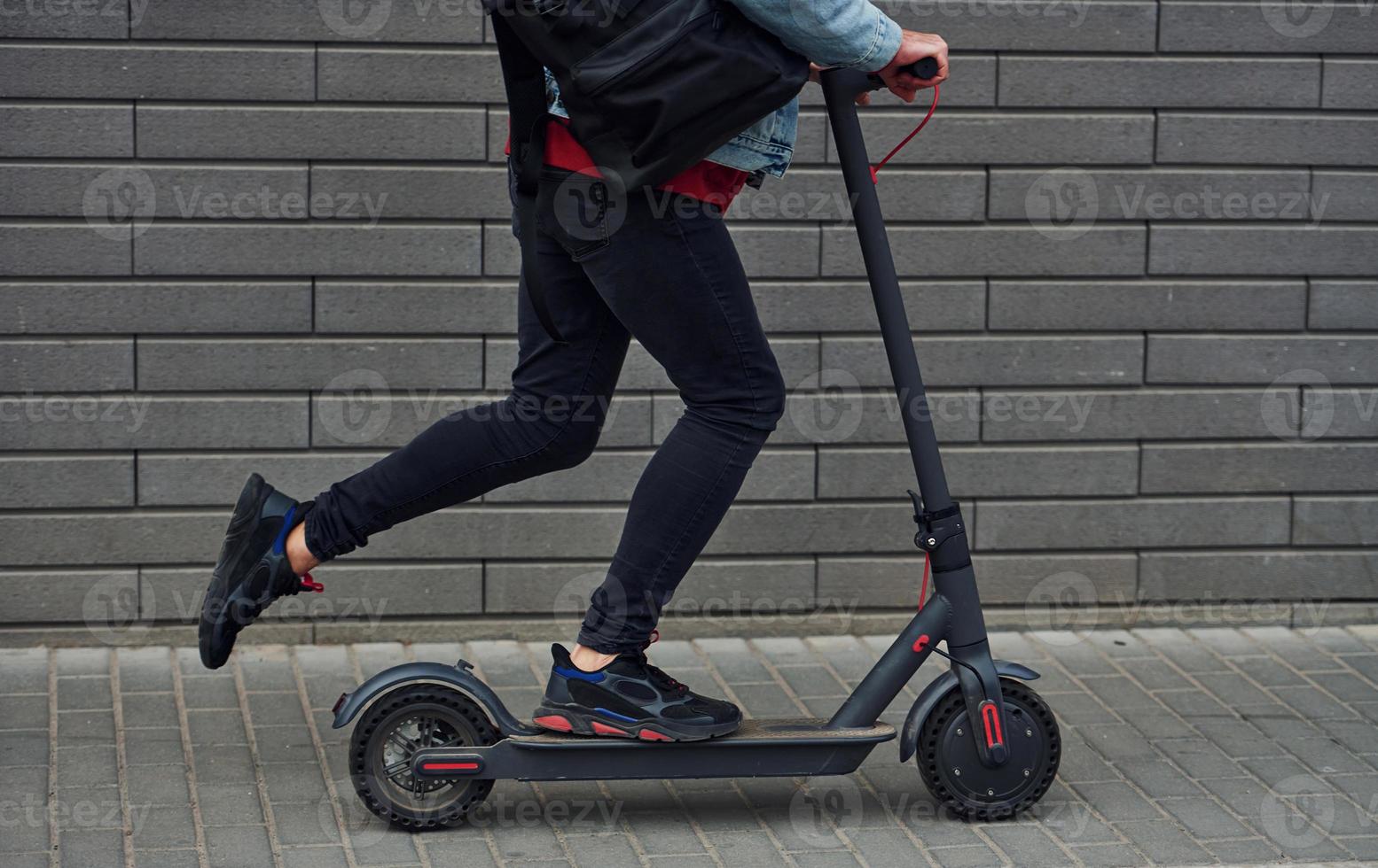 Vista de cerca de un tipo con ropa informal que monta un scooter eléctrico al aire libre durante el día soleado foto