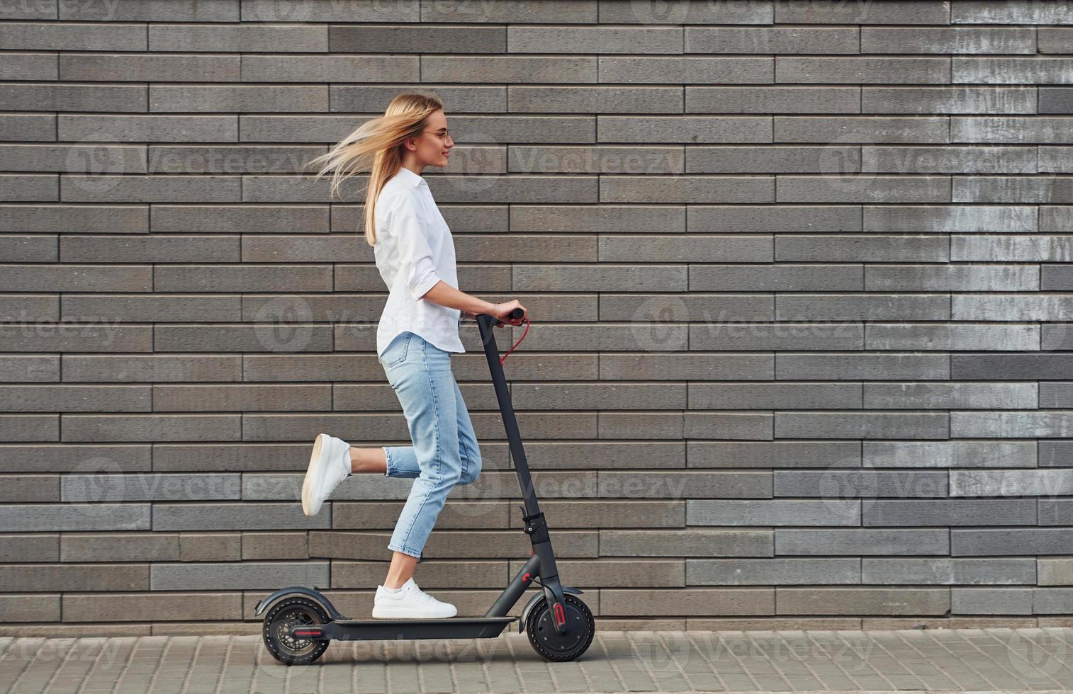 Side View Of Beautiful Blonde In Casual Clothes That Riding Electric Schooter Outdoors At Sunny