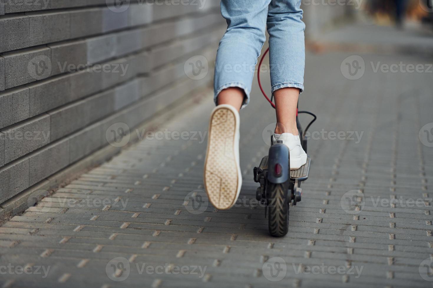 Close up view of girl in casual clothes that riding electric schooter outdoors at sunny daytime photo