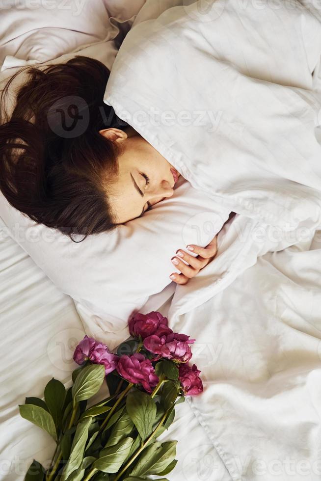 Lying down on bed with flowers. Young woman resting and spending weekend at home alone at home photo