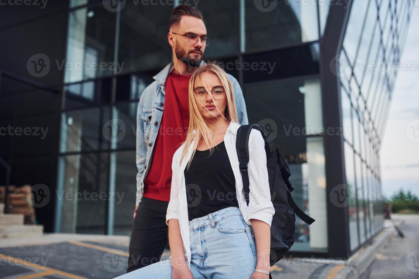 Young stylish man with woman in casual clothes outdoors together near business building. Conception of friendship or relationships photo