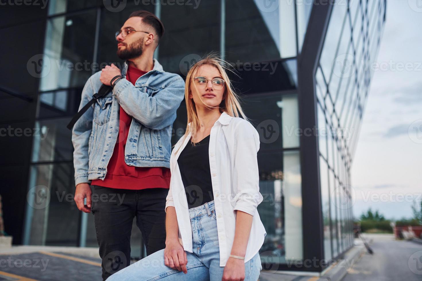 Young stylish man with woman in casual clothes outdoors together near business building. Conception of friendship or relationships photo
