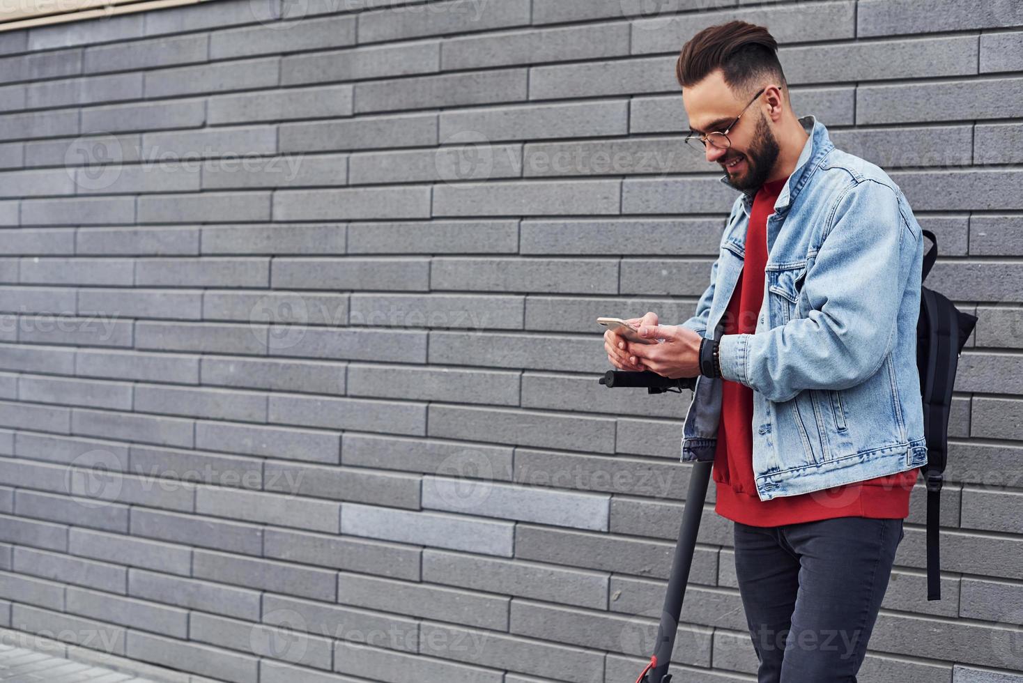 Handsome young guy in casual clothes riding electric schooter outdoors at sunny daytime photo