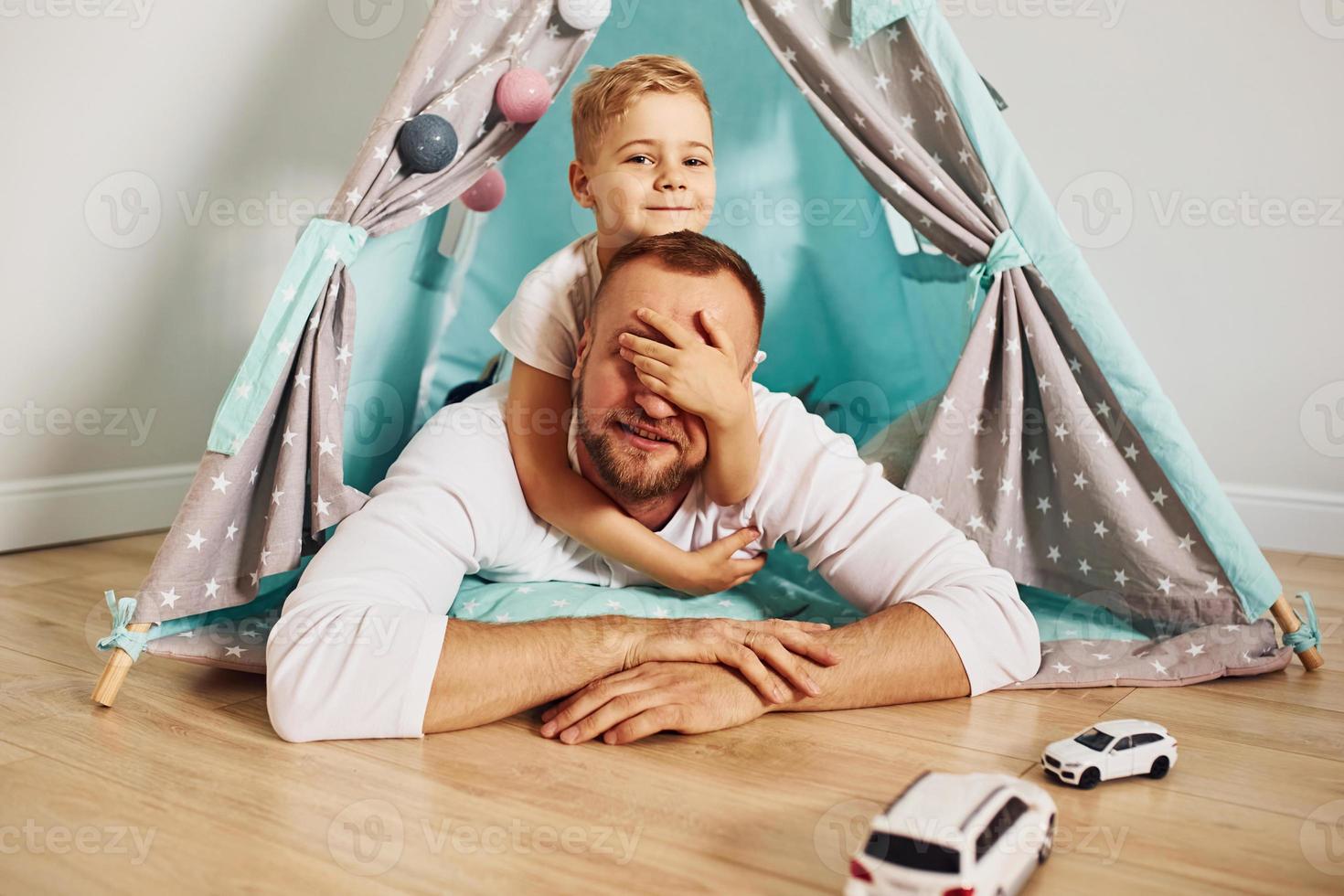 With toy cars. Father and his young young spending time together indoors near tent photo