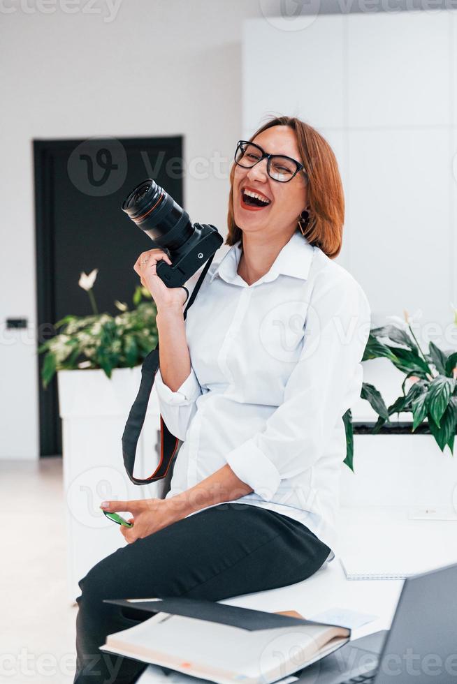 Woman in formal clothes and with camera sitting in the office photo
