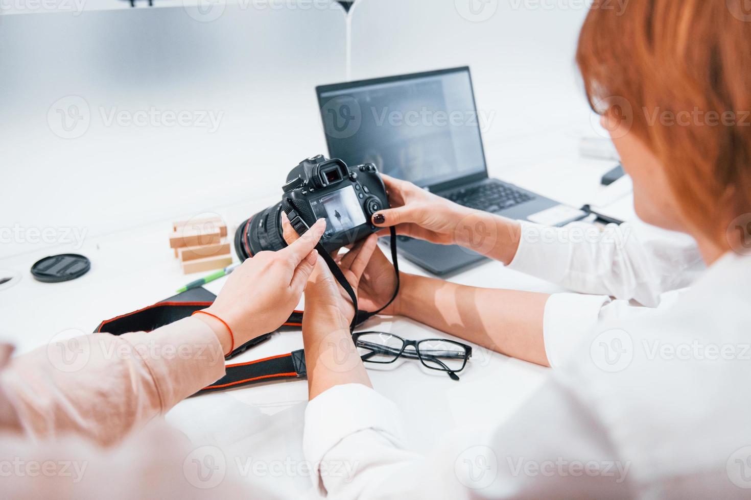 Two women sitting by the table and looking at photos that is in camera