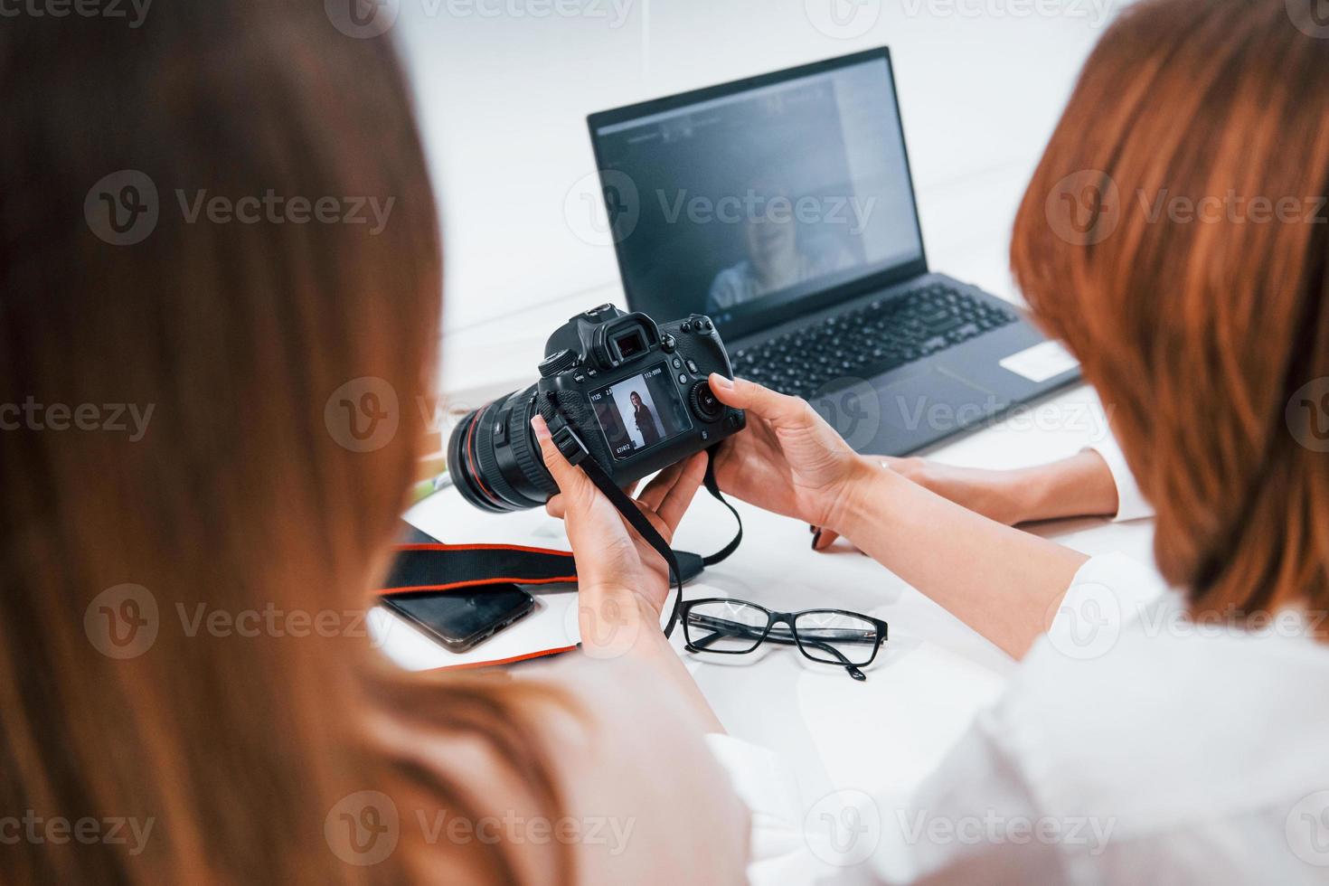 Two women sitting by the table and looking at photos that is in camera