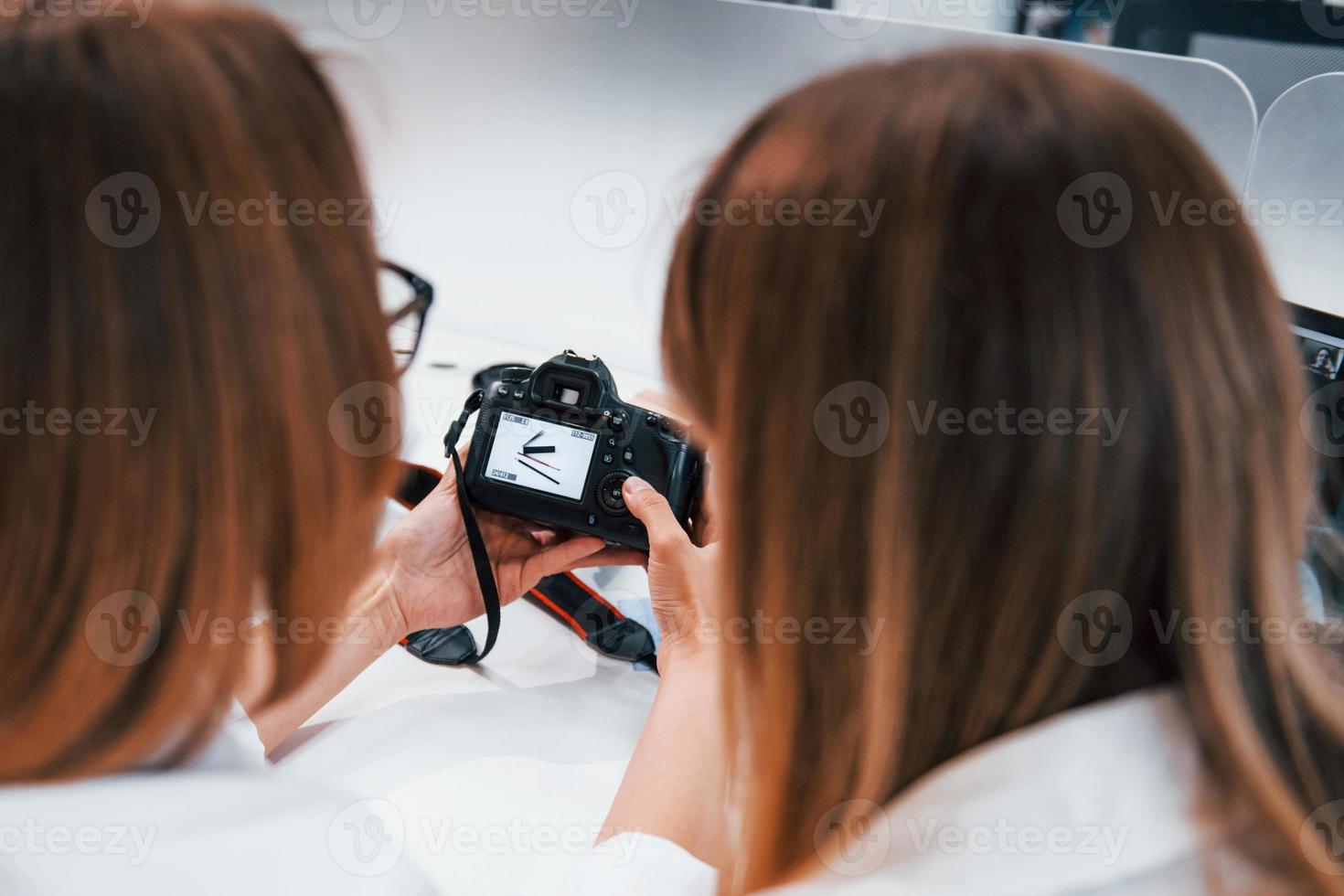 Two women sitting by the table and looking at photos that is in camera