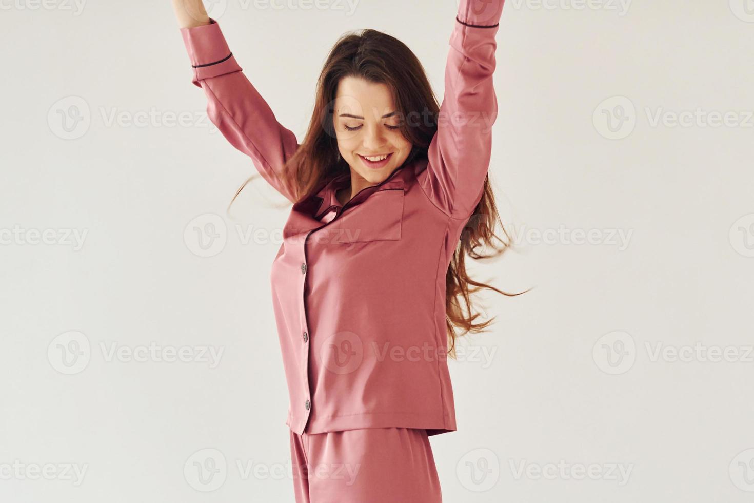 Cheerful young woman in pajamas standing indoors against white background in the studio photo