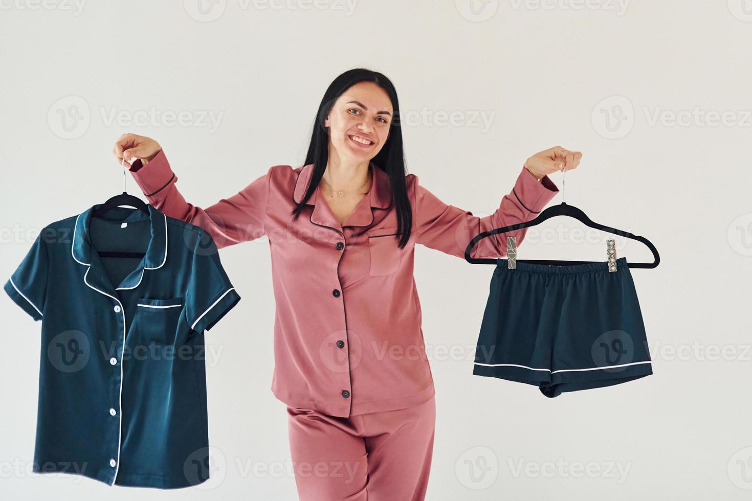 sosteniendo ropa azul en las manos. mujer joven alegre en pijama de pie en el interior durante el día foto