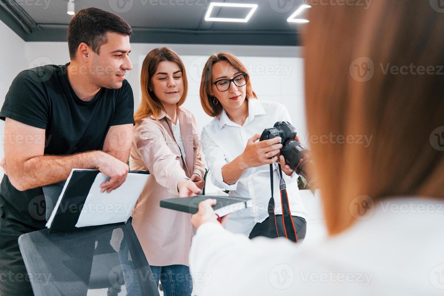 Group of business people in formal clothes indoors in the office looking at photos on the camera