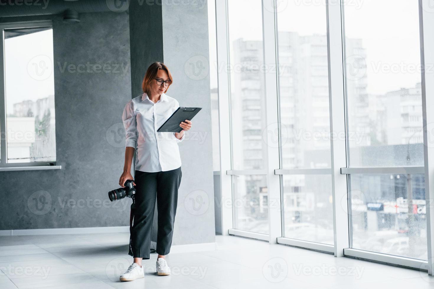 Woman in formal clothes and with camera in hand standing inside of empty room photo