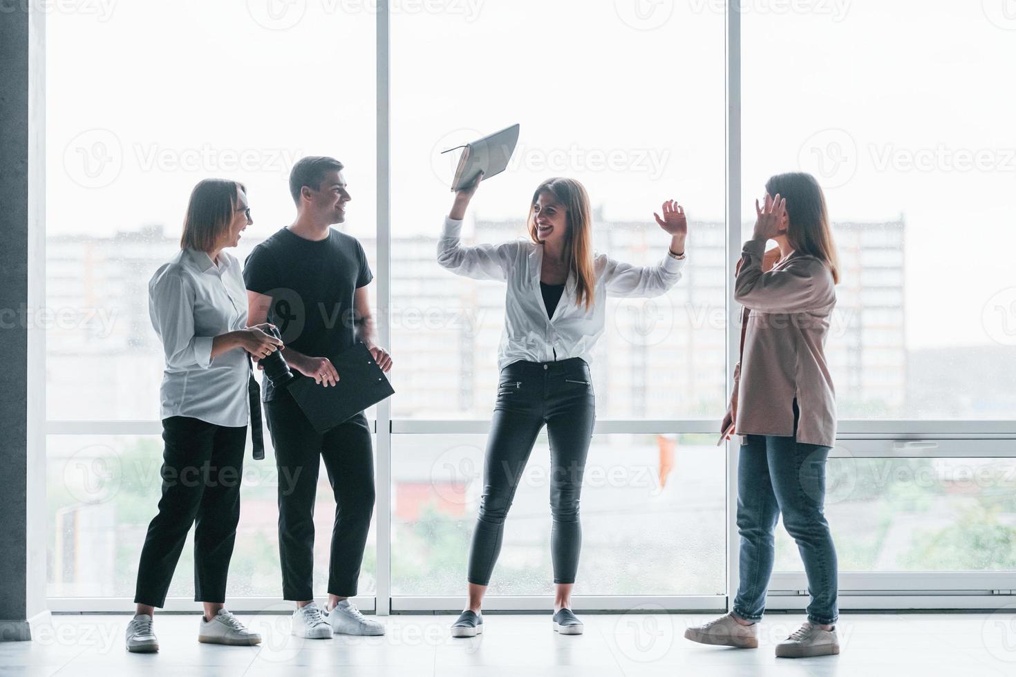 Woman holding her professional camera. Group of business people in formal clothes standing indoors near big window photo