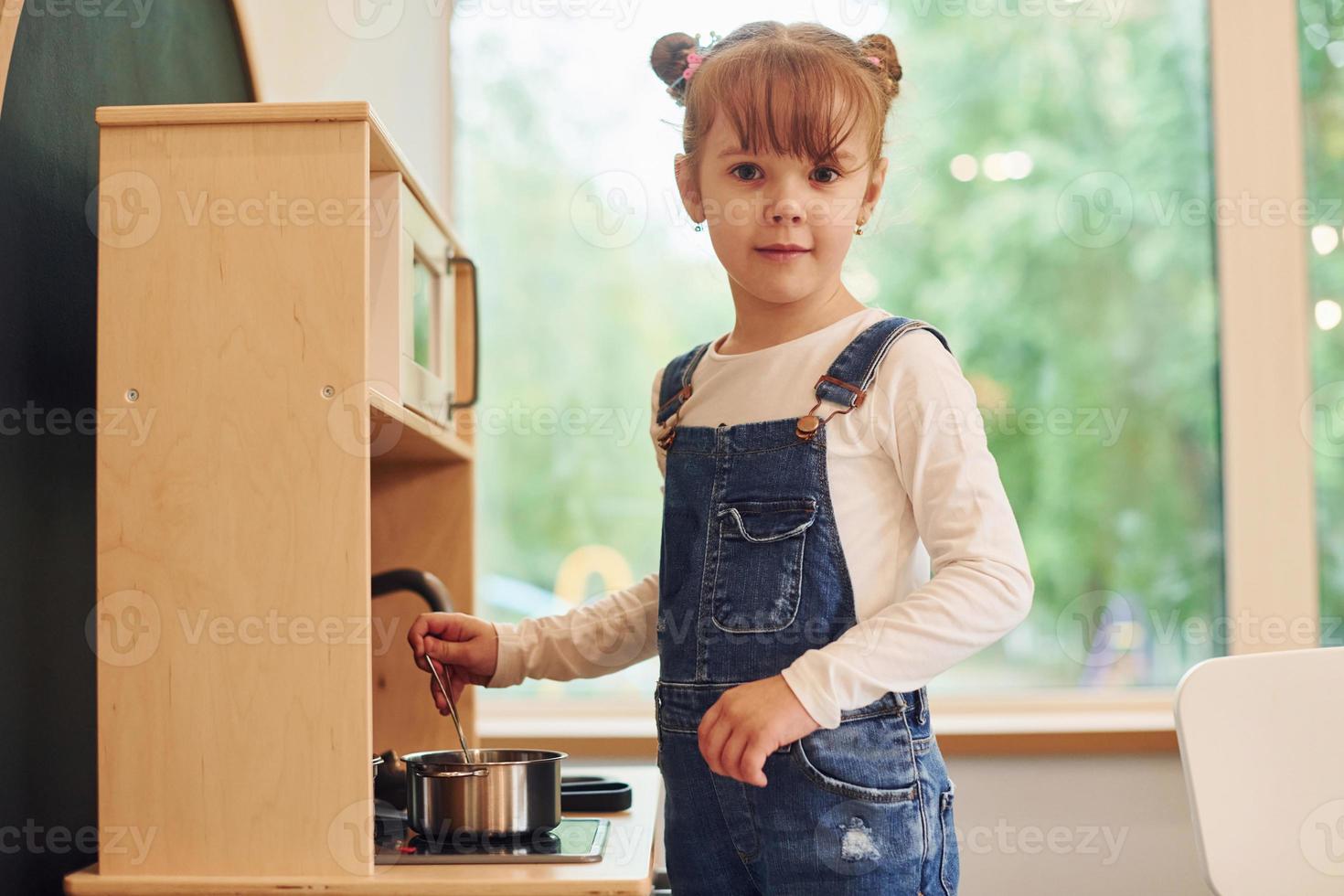 Little girl in casual clothes have fun by playing with toys on the kitchen photo