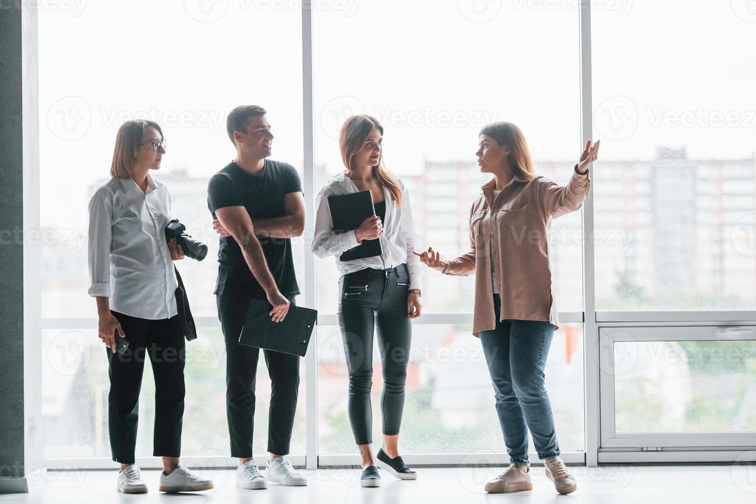 Woman holding her professional camera. Group of business people in formal clothes standing indoors near big window photo