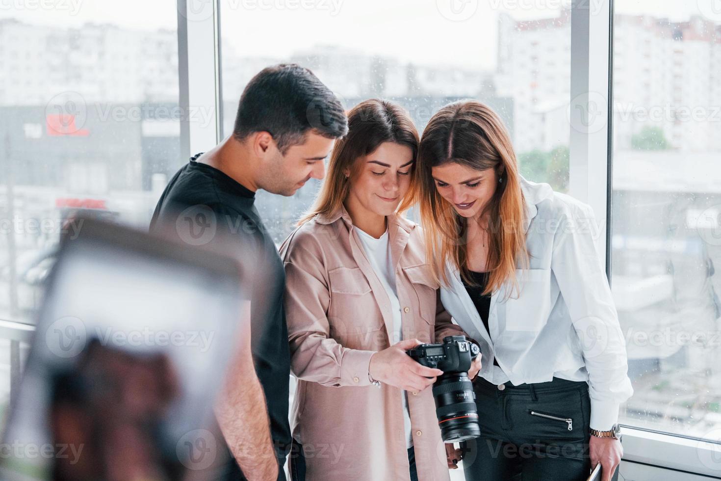 Group of people standing indoors together and looks at photos on camera