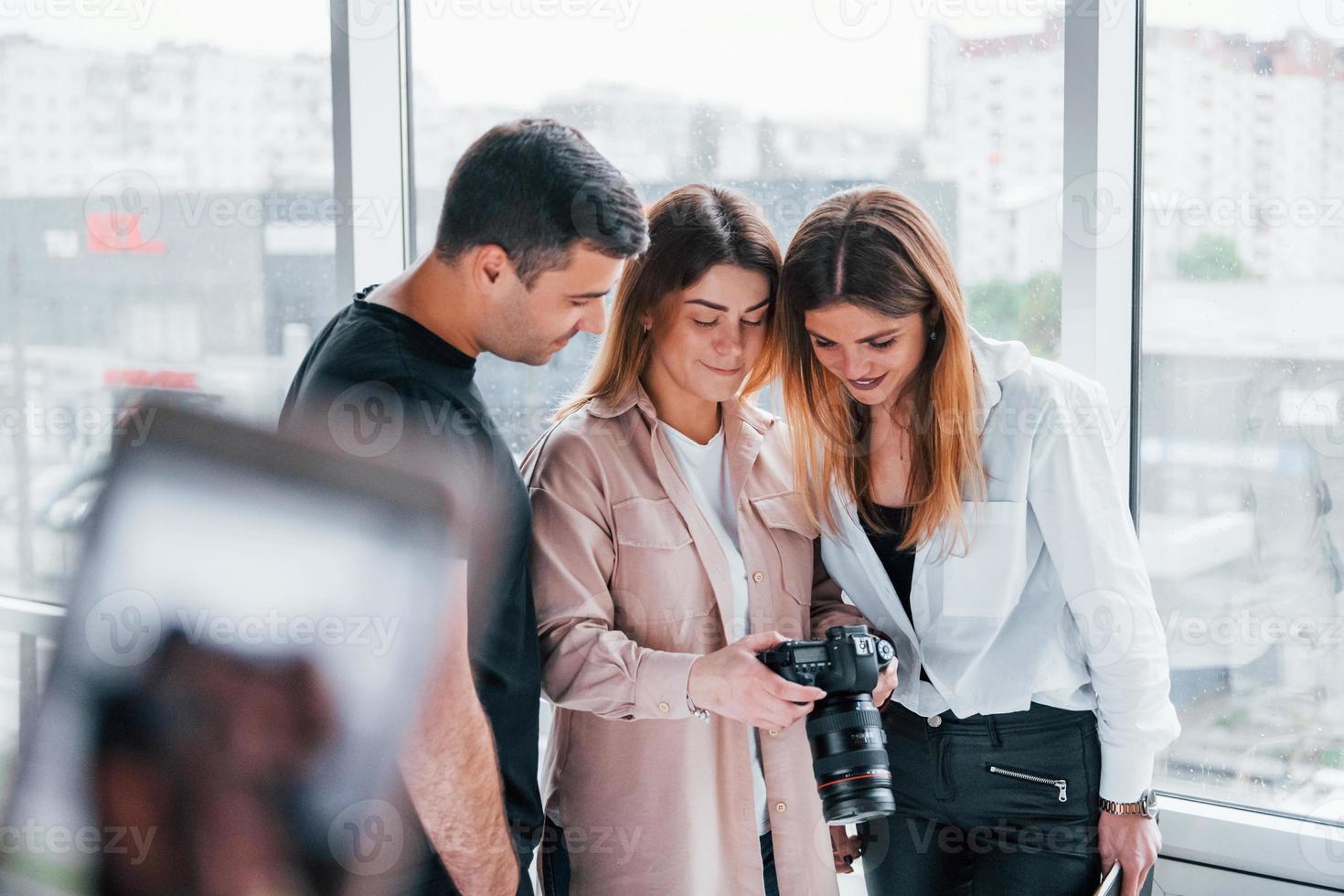 Group of people standing indoors together and looks at photos on camera