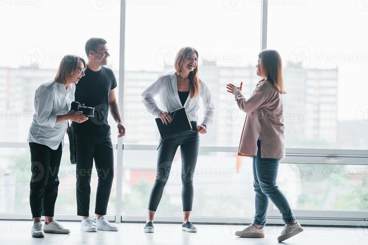 Woman holding her professional camera. Group of business people in formal clothes standing indoors near big window photo