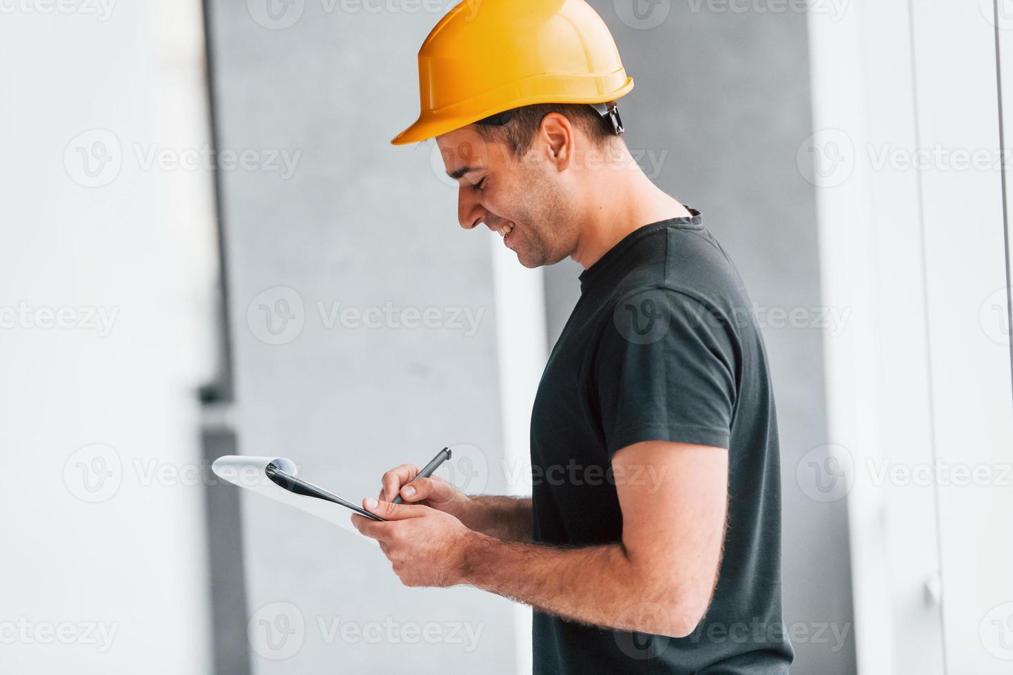 Male worker or engineer in yellow hard hat standing indoors with notepad photo