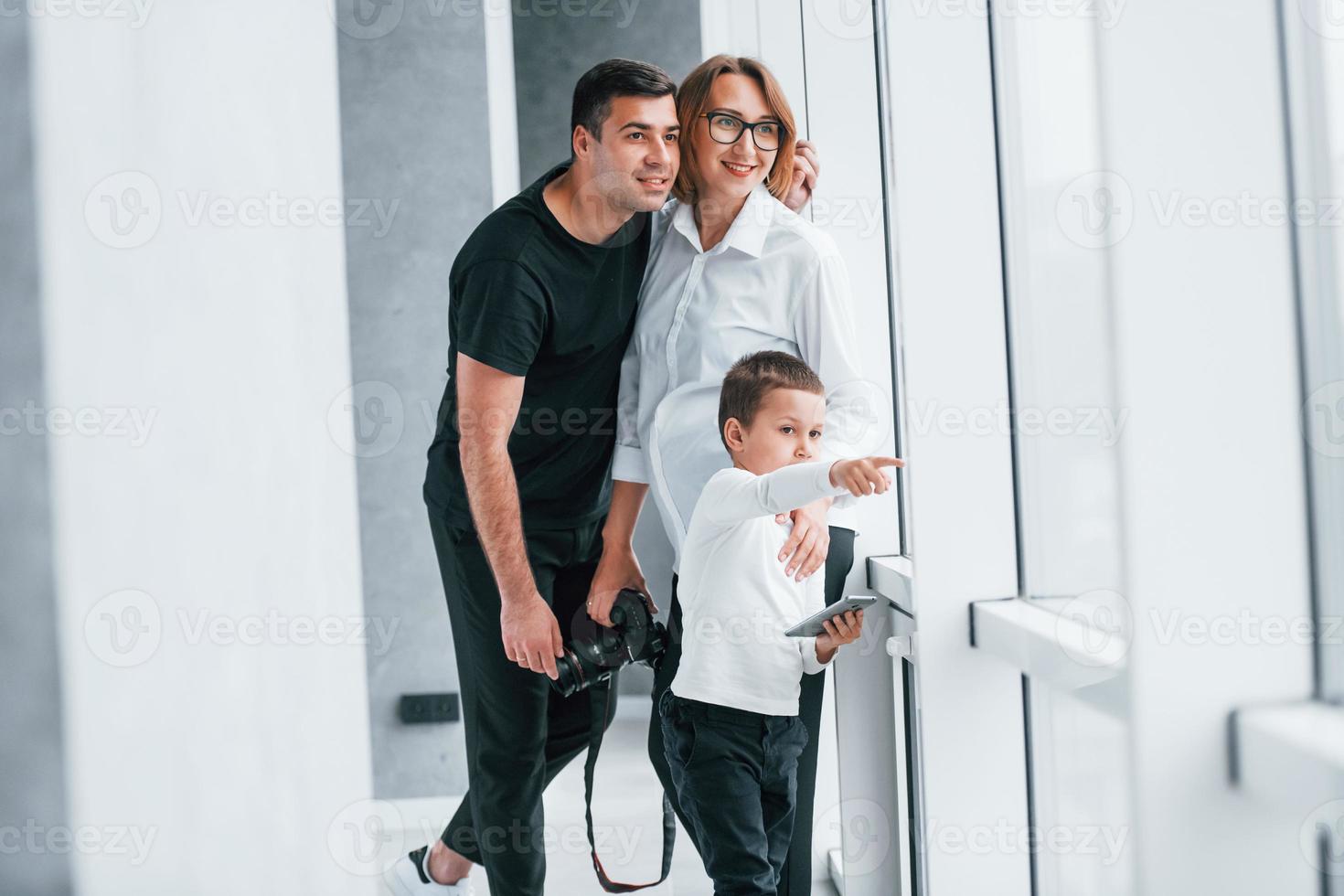 Woman in formal clothes and with camera in hand standing inside of empty room with man and little boy photo