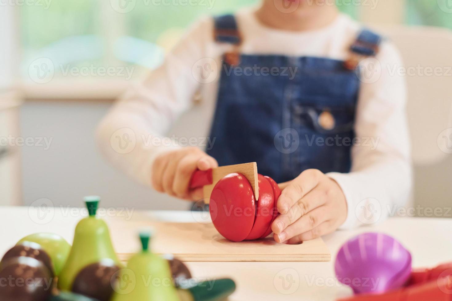 Close up view of little girl in casual clothes that have fun by playing with toys on the kitchen photo