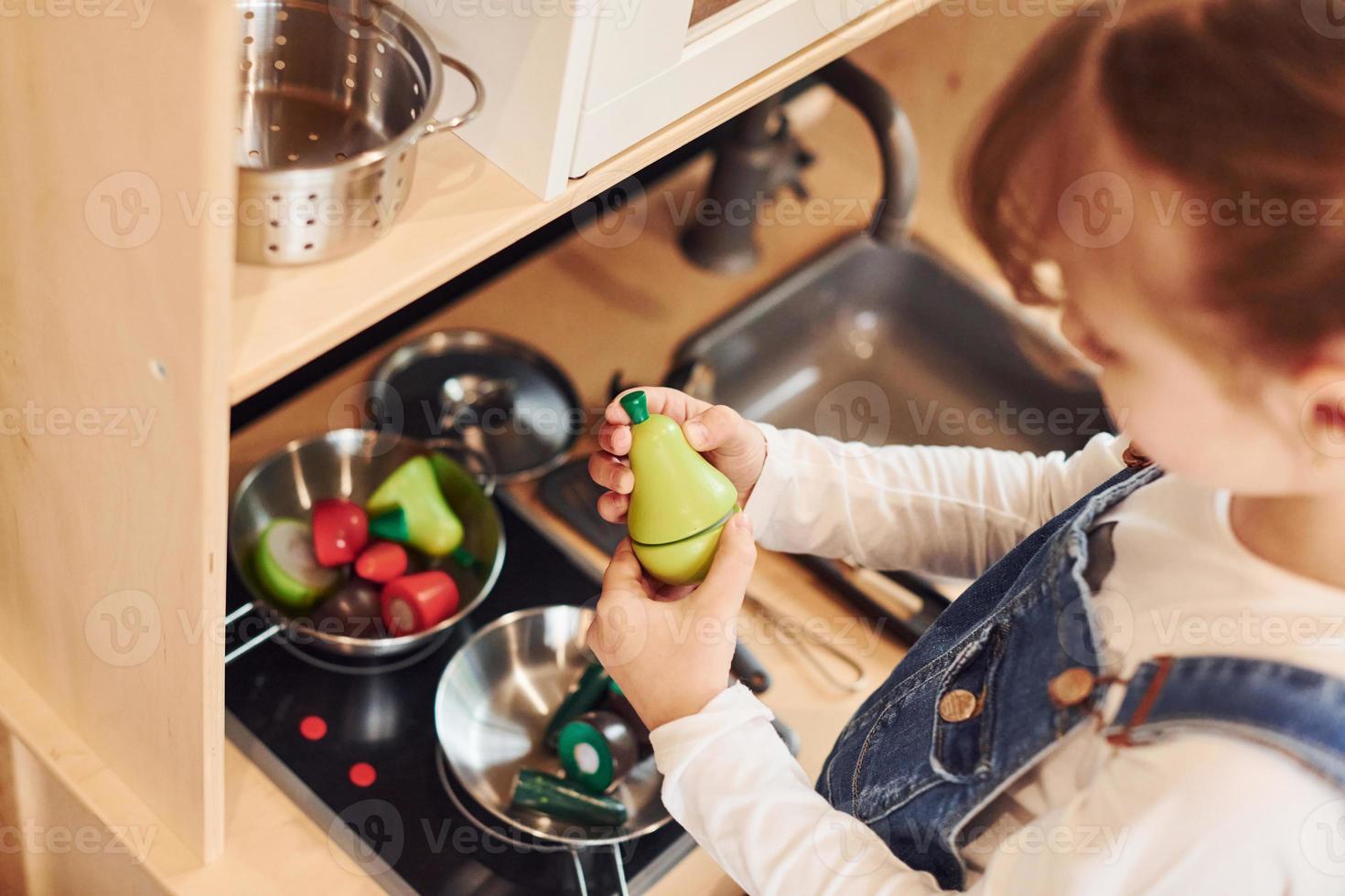 Little girl in casual clothes have fun by playing with toys on the kitchen photo