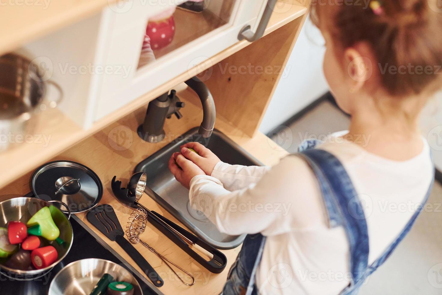 Little girl in casual clothes have fun by playing with toys on the kitchen photo