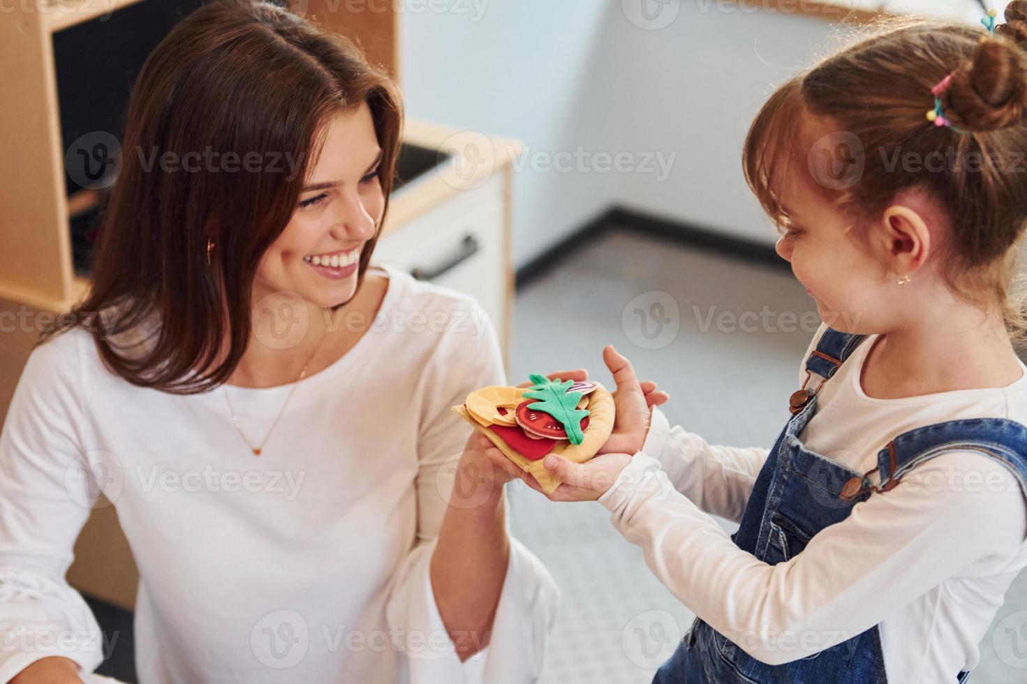 Young woman with little girl playing with toys together on the kitchen photo