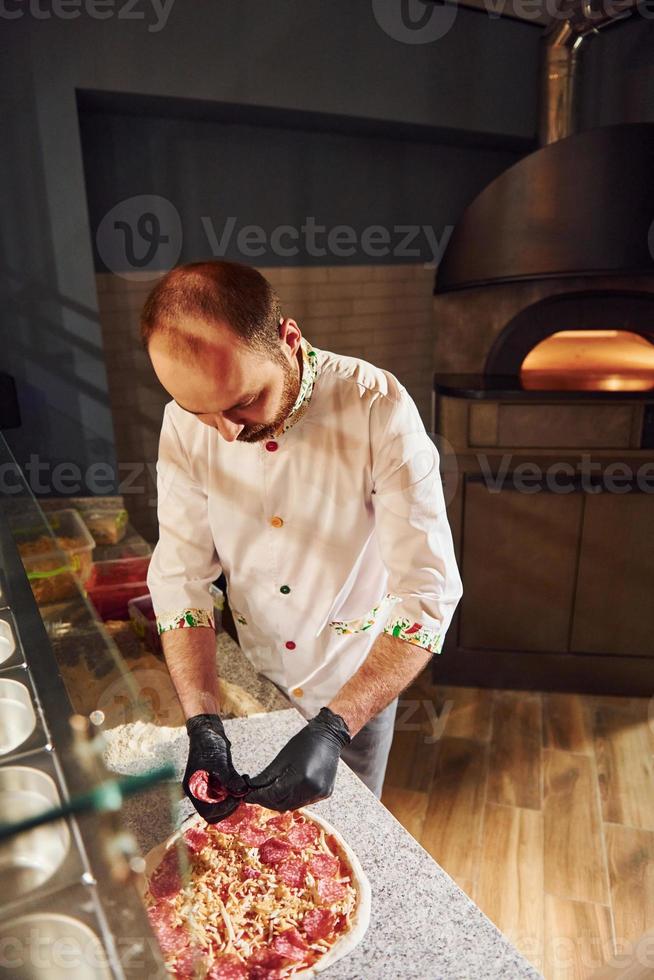 chef vestido de blanco preparando deliciosa pizza en la cocina del restaurante foto