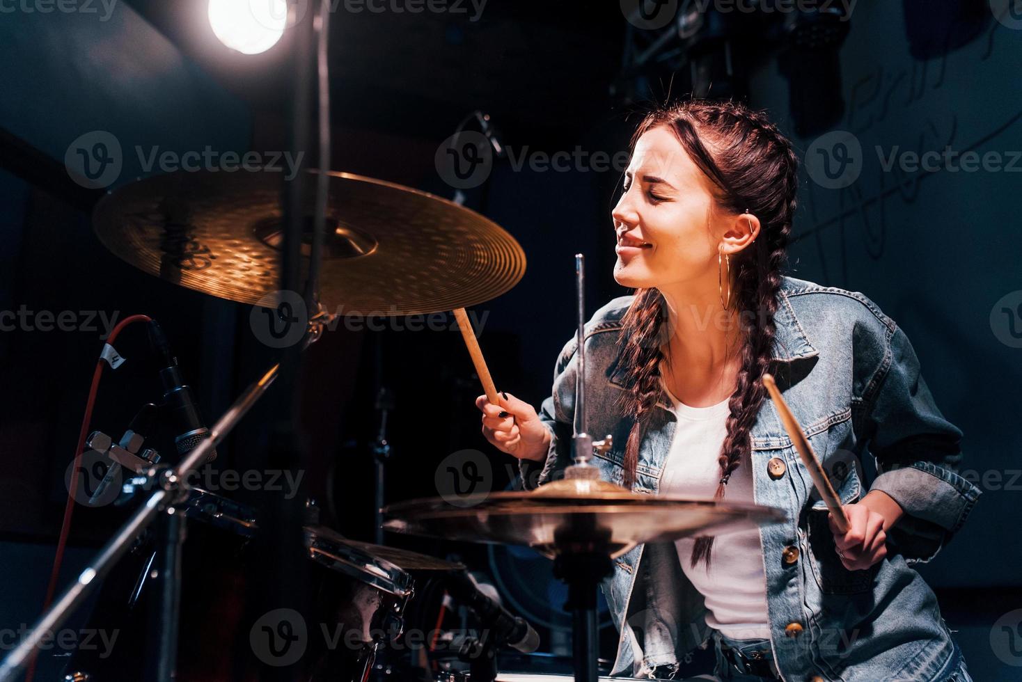 Plays drums. Young beautiful female performer rehearsing in a recording studio photo