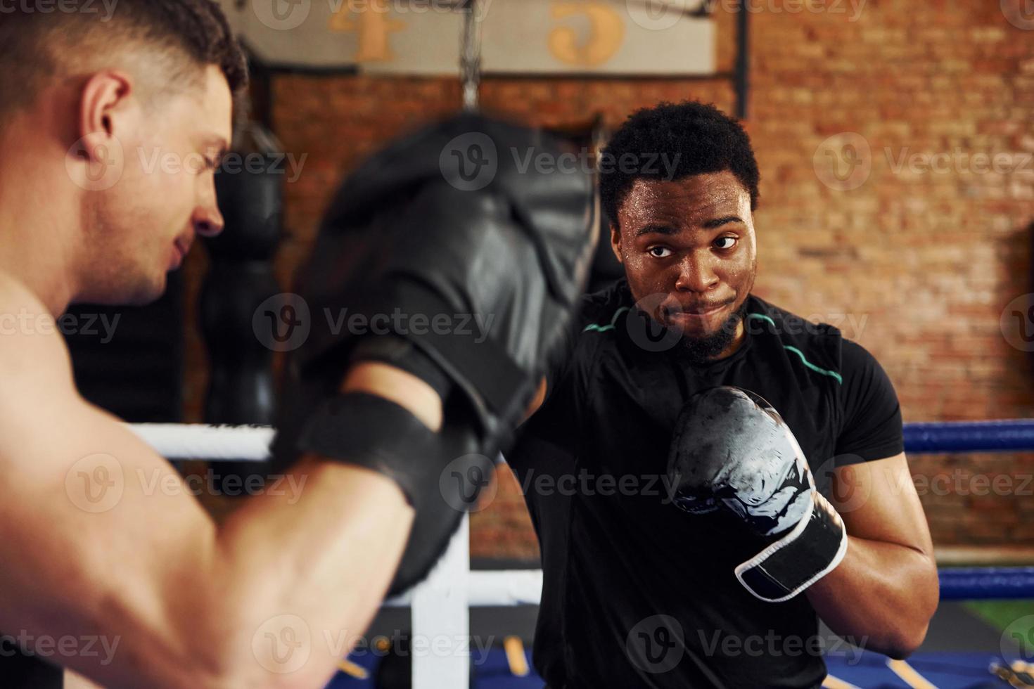 tener el boxeo practicando. un hombre afroamericano con un hombre blanco tiene un día de entrenamiento en el gimnasio foto