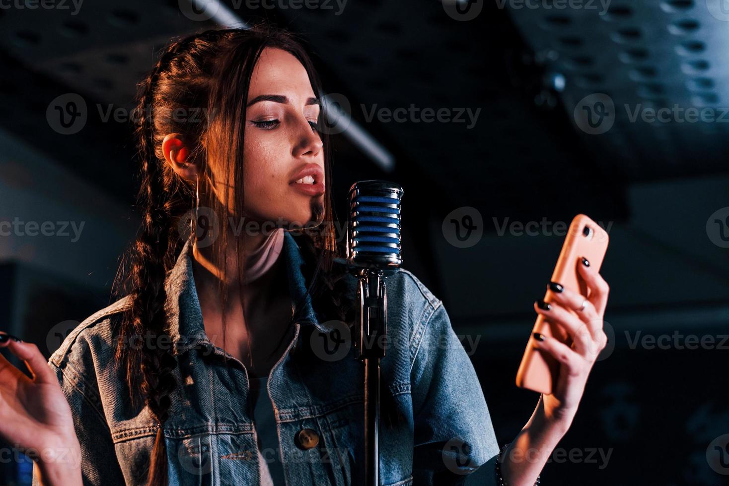 Holding smartphone. Young beautiful female performer rehearsing in a recording studio photo