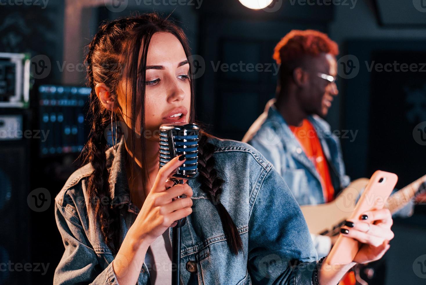 el chico toca la guitarra, la chica canta. hombre afroamericano con chica blanca ensayando juntos en el estudio foto