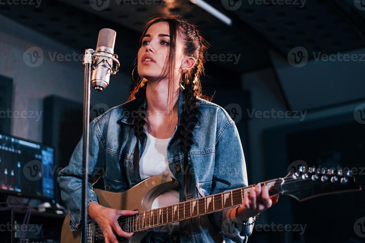 Young beautiful female performer with guitar singing and rehearsing in a recording studio photo