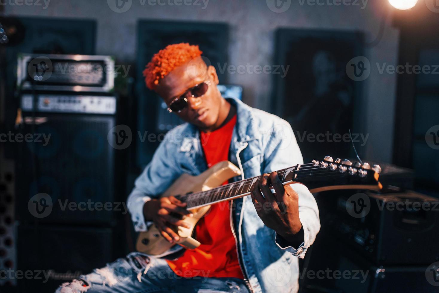 Plays guitar. Young african american performer rehearsing in a recording studio photo