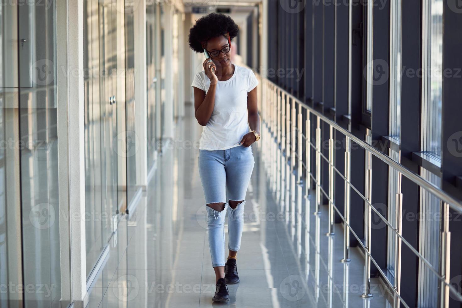 una joven pasajera afroamericana con ropa informal está en el aeropuerto con teléfono foto
