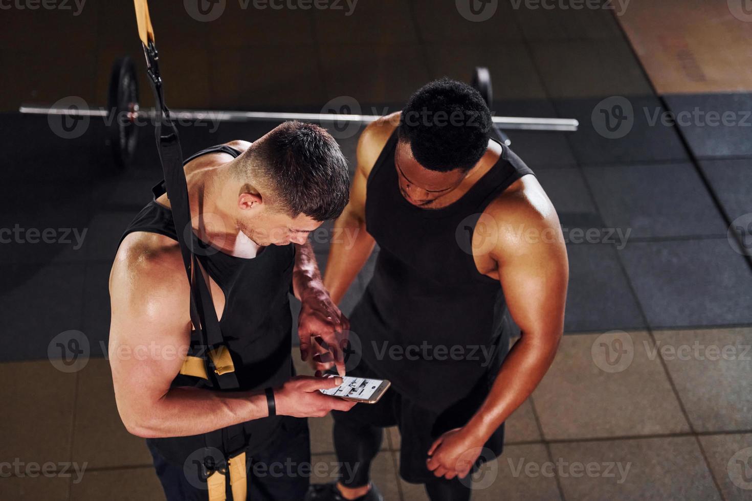 Taking a break and using phone. African american man with white guy have workout day in gym photo